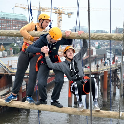 Drei Jugendliche helfen sich in gro�er H�he bei der Bew�ltigung eines Balancierelements