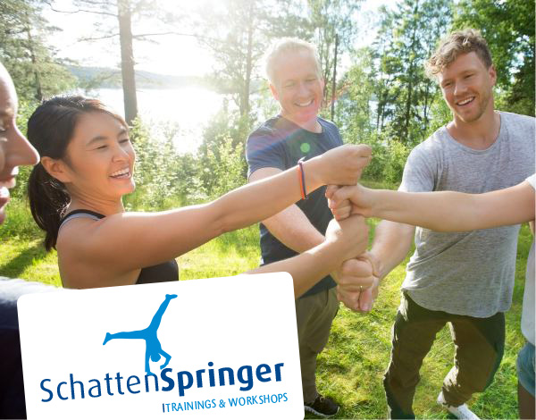 Ein Team steht im Kreis und bildet gemeinsam mit ihren F�usten einen Turm - Dazu wird das Logo von Schattenspringer Trainings und Workshops eingeblendet